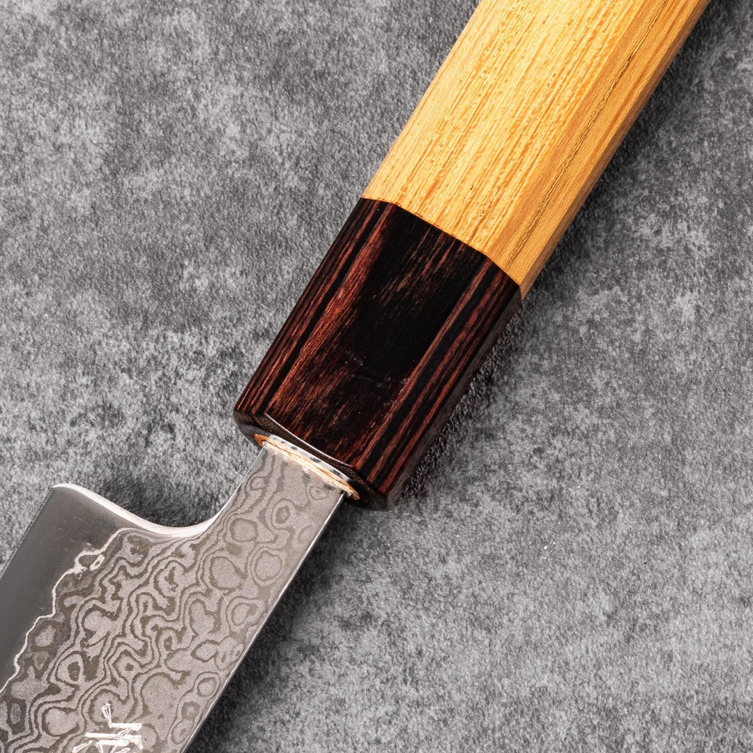 Japanese Damascus petty knife with intricate layered steel blade and natural wood handle placed on gray stone surface.