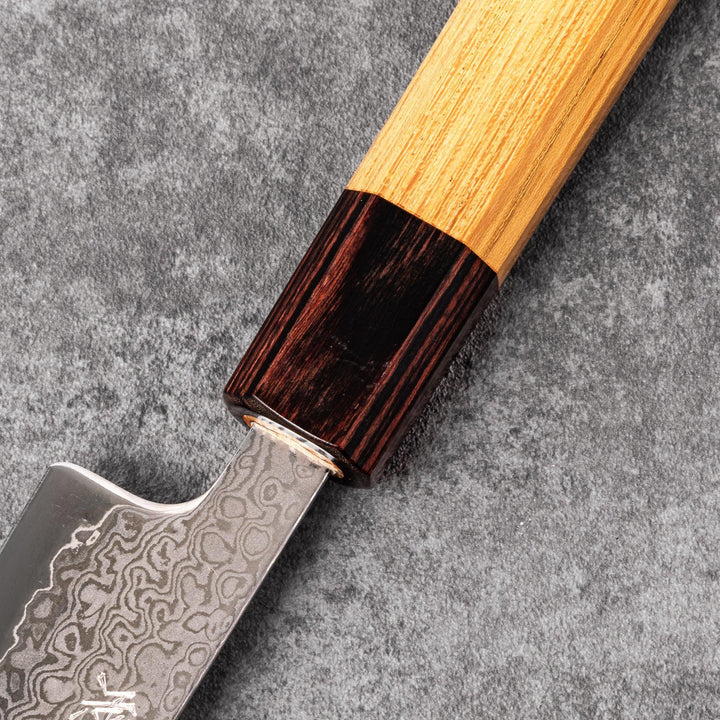 Japanese Damascus petty knife with intricate layered steel blade and natural wood handle placed on gray stone surface.