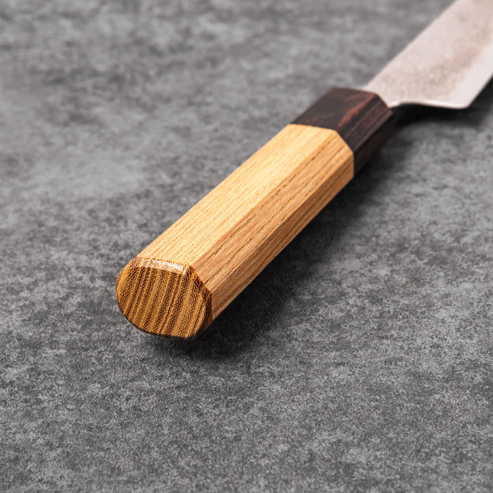 Japanese Damascus petty knife with intricate layered steel blade and natural wood handle placed on gray stone surface.