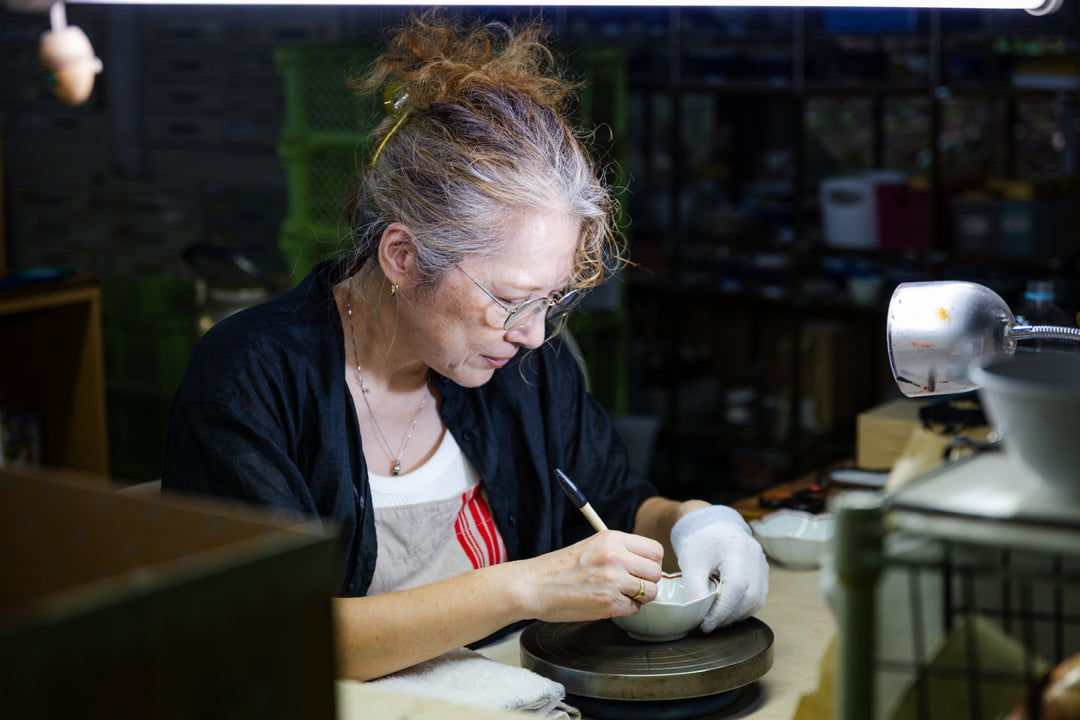 Artisan carefully hand-painting a ceramic bowl in a workshop, adding detailed brushwork under soft task lighting.