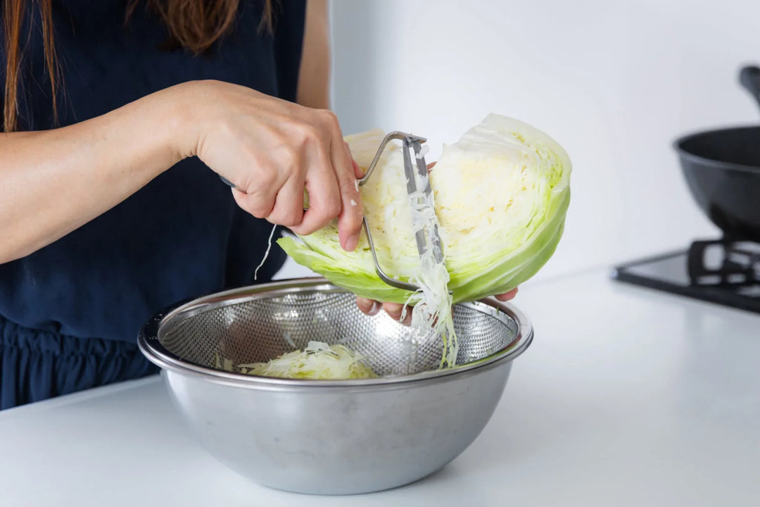 Shredding fresh cabbage with a Japanese stainless steel slicer over a fine mesh mixing bowl in a home kitchen
