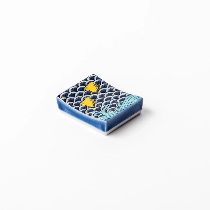 Rectangular Japanese ceramic chopstick rest with blue wave pattern and yellow shorebirds for traditional dining.