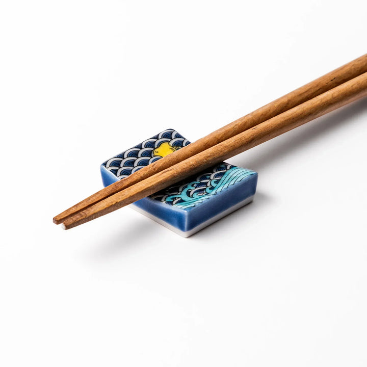 Rectangular Japanese ceramic chopstick rest with blue wave pattern and yellow shorebirds for traditional dining.