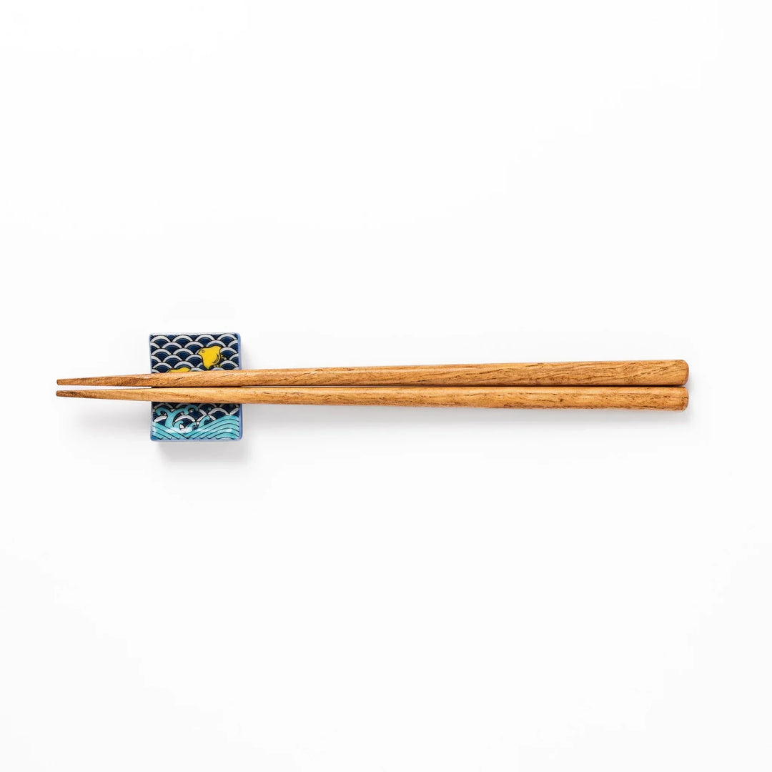 Rectangular Japanese ceramic chopstick rest with blue wave pattern and yellow shorebirds for traditional dining.