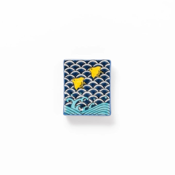 Rectangular Japanese ceramic chopstick rest with blue wave pattern and yellow shorebirds for traditional dining.