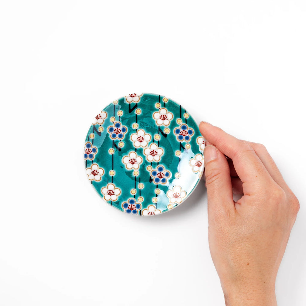 Round Japanese ceramic sauce dish with teal background and white blue plum blossom motifs for condiments.