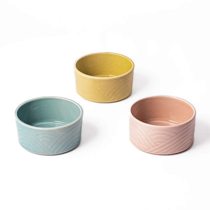 Three medium Japanese porcelain bowls in pastel blue yellow and pink with embossed Seigaiha wave pattern.