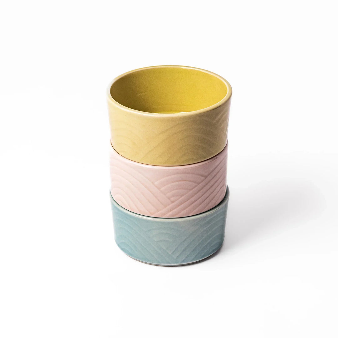 Set of three small Japanese porcelain bowls in yellow pink and blue with embossed Seigaiha wave pattern.