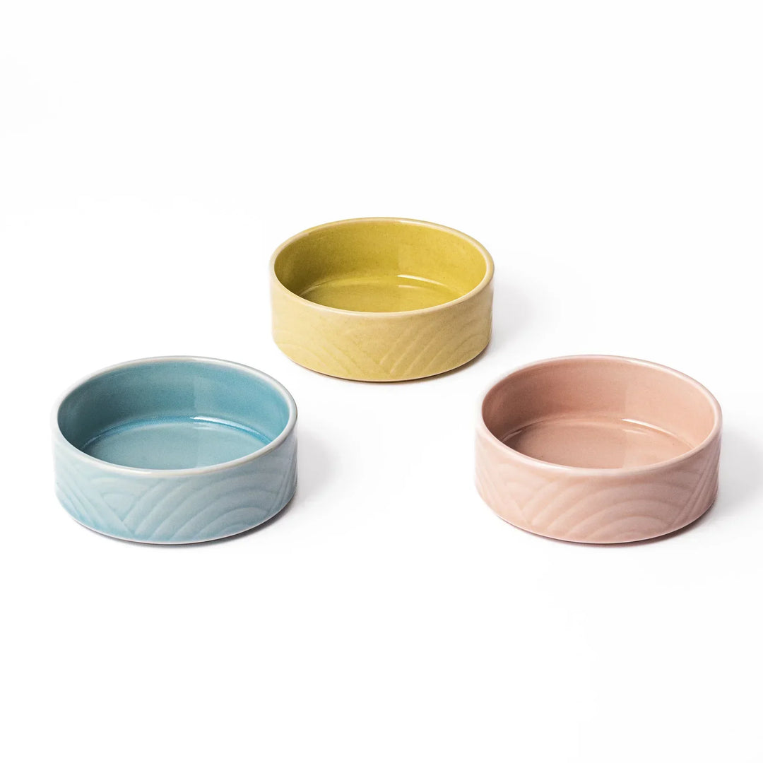 Set of three small Japanese porcelain bowls in yellow pink and blue with embossed Seigaiha wave pattern.