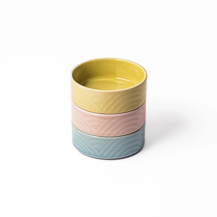 Set of three small Japanese porcelain bowls in yellow pink and blue with embossed Seigaiha wave pattern.