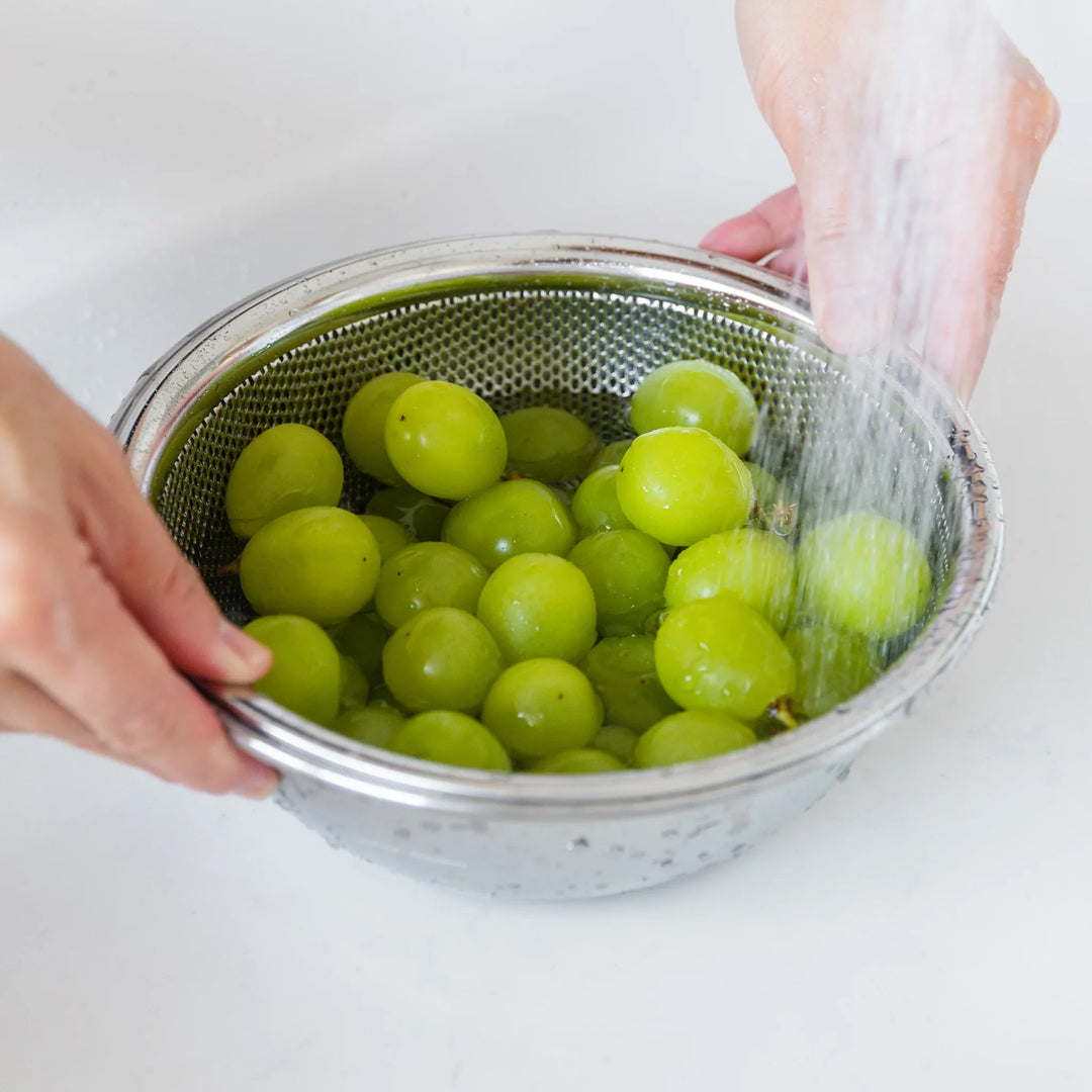 Green grapes being rinsed in a metal colander with hands holding it.