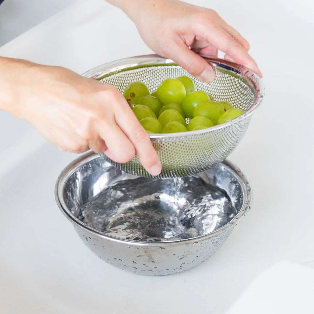 Nami sorting green grapes into a metal colander over a bowl on a white surface