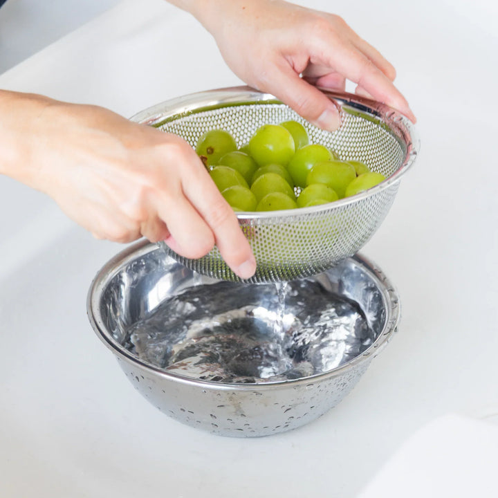 Nami sorting green grapes into a metal colander over a bowl on a white surface