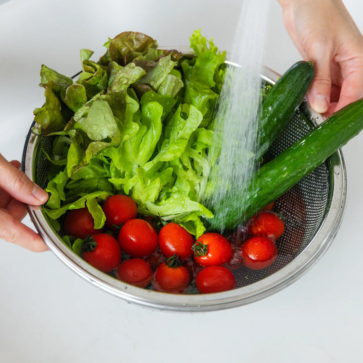 Washed lettuce and tomatoes draining in a colander over a bowl, showing efficient rinsing and straining in kitchen workflow.