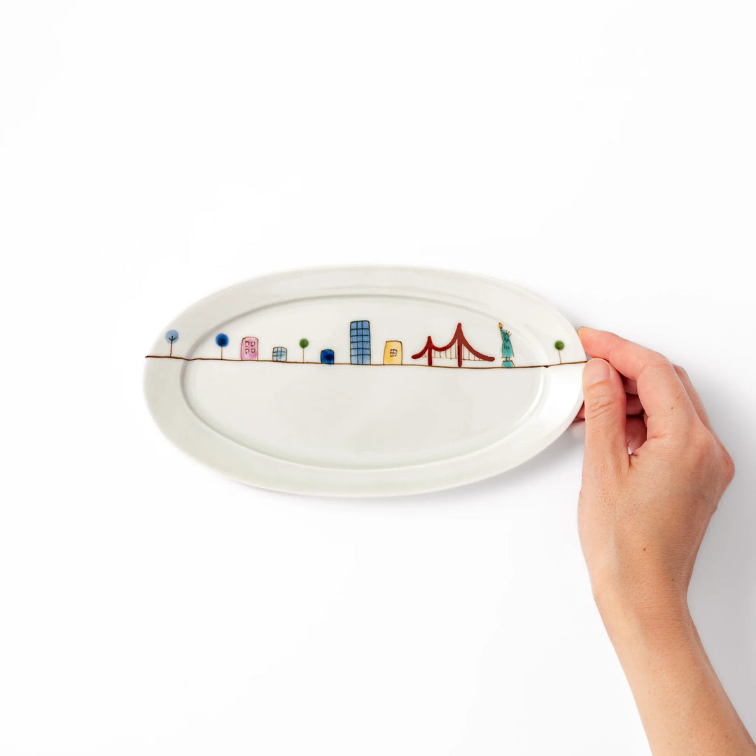 Japanese porcelain oval plate with playful USA cityscape design featuring Statue of Liberty, bridge, and colorful buildings