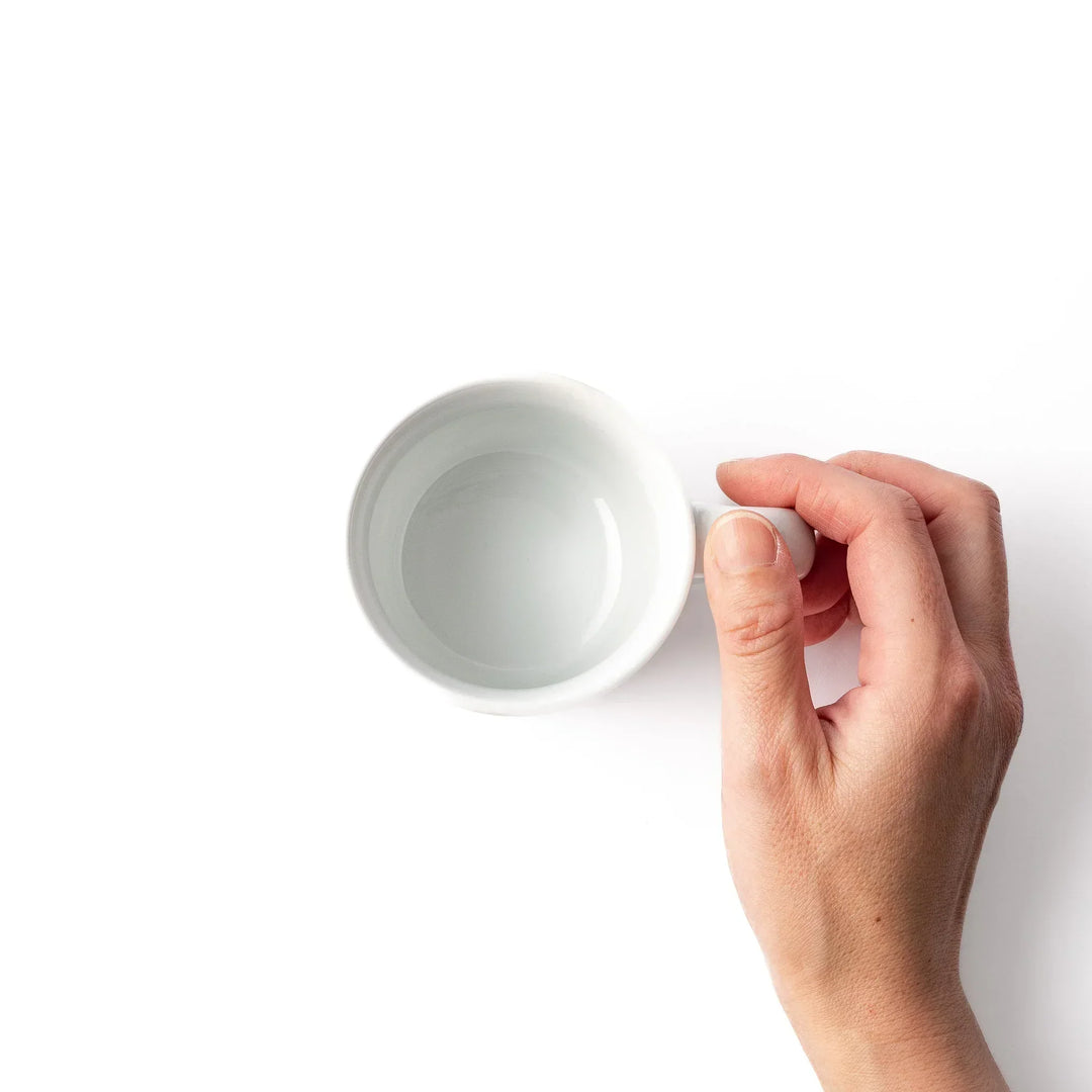 White ceramic kids mug featuring green T-Rex dinosaur graphic with yellow accents and blue cloud motifs, round handle