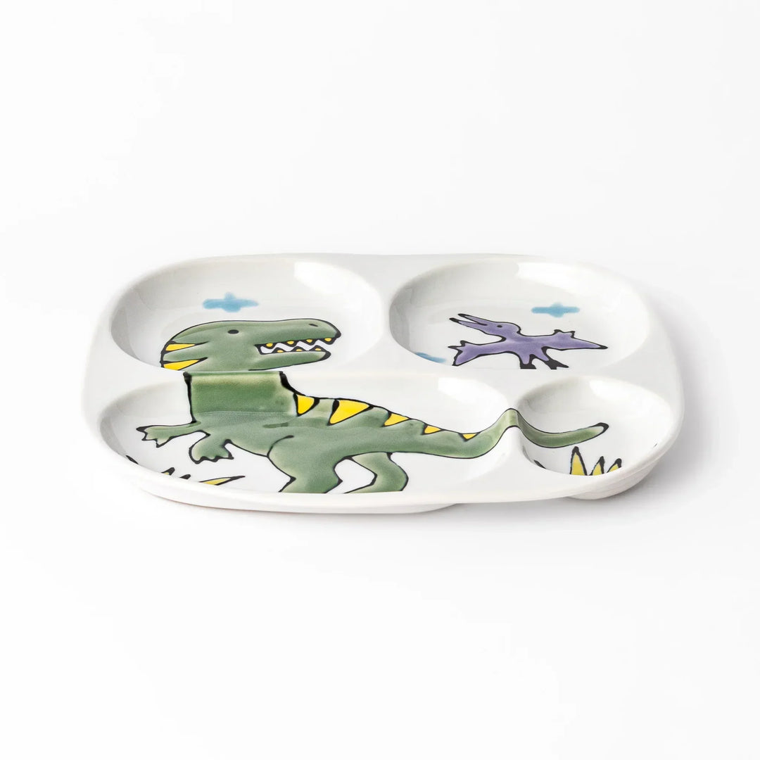 White ceramic kids divided plate with green T-Rex, purple pterodactyl, yellow grass and blue cloud accents
