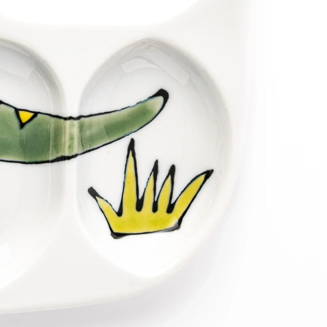 White ceramic kids divided plate with green T-Rex, purple pterodactyl, yellow grass and blue cloud accents