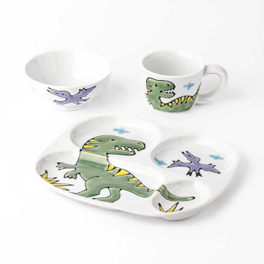White ceramic kids mug, divided plate and rice bowl set featuring green T-Rex dinosaur graphics and blue cloud accents