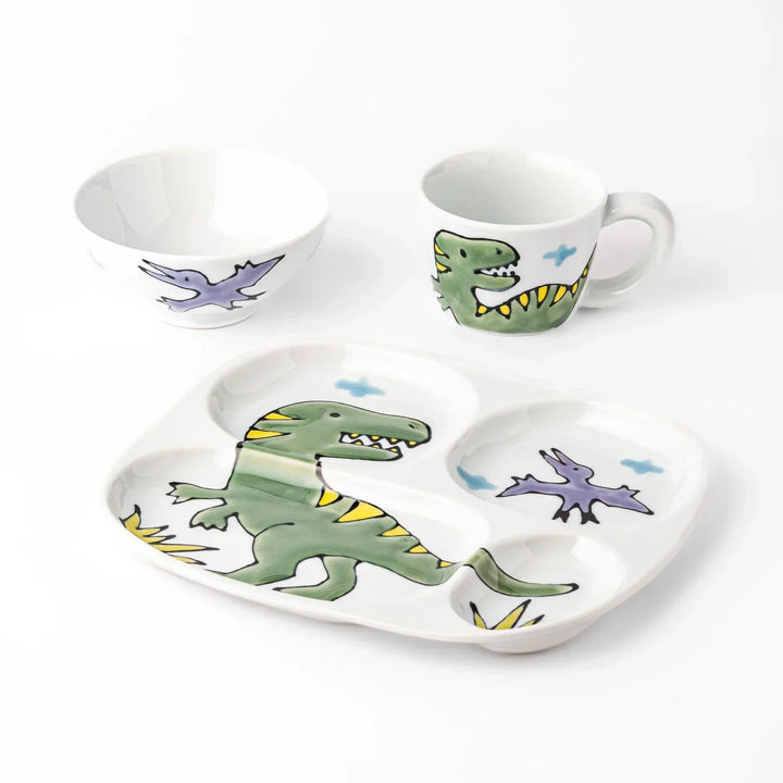 White ceramic kids mug, divided plate and rice bowl set featuring green T-Rex dinosaur graphics and blue cloud accents