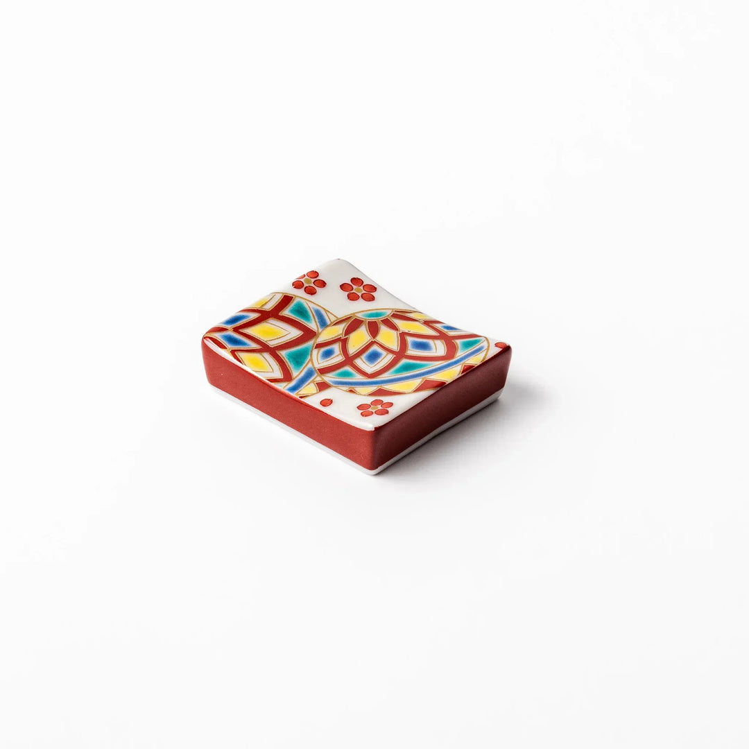 Rectangular Japanese ceramic chopstick rest with colorful temari ball and red floral patterns for dining.