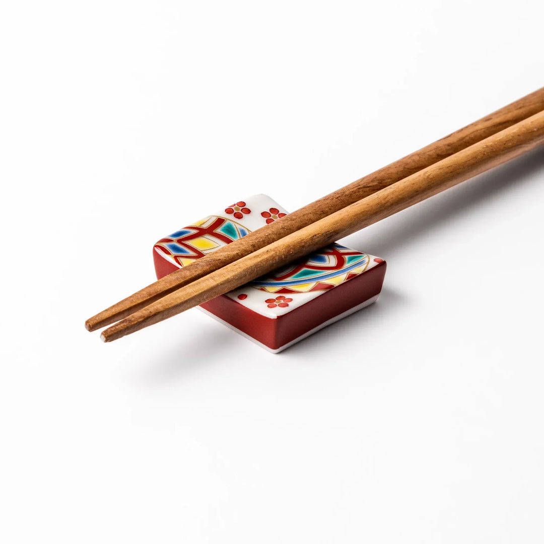 Rectangular Japanese ceramic chopstick rest with colorful temari ball and red floral patterns for dining.
