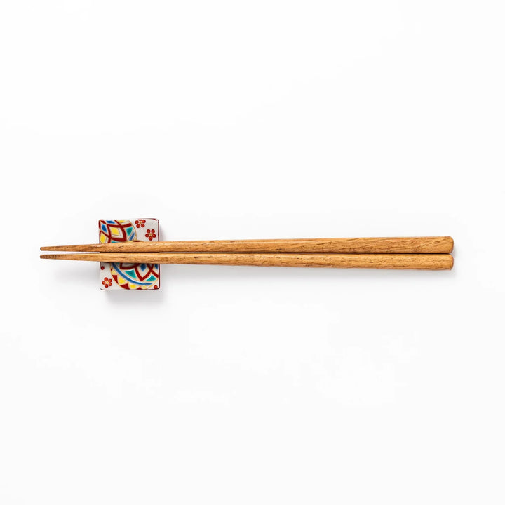 Rectangular Japanese ceramic chopstick rest with colorful temari ball and red floral patterns for dining.