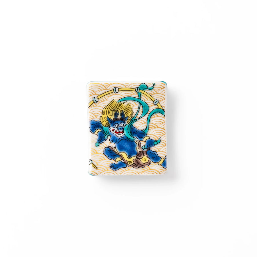 Japanese porcelain chopstick rest featuring the Thunder God design with blue figure and gold wave pattern background.