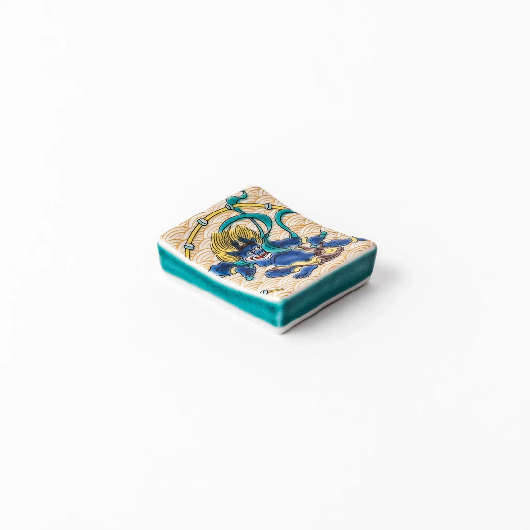 Japanese porcelain chopstick rest featuring the Thunder God design with blue figure and gold wave pattern background.