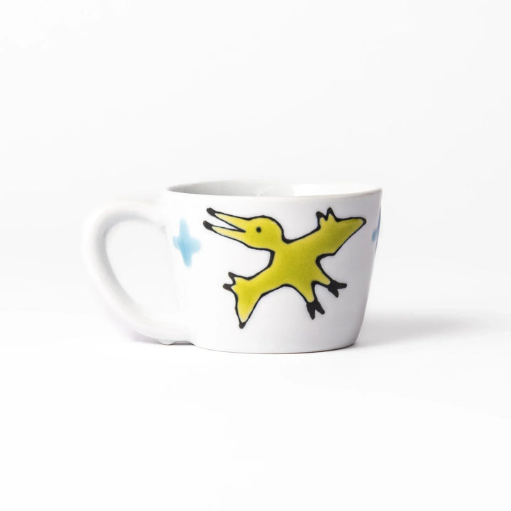 White ceramic kids mug with blue triceratops graphic, yellow horns and stripes, plus blue cloud accents, round handle.
