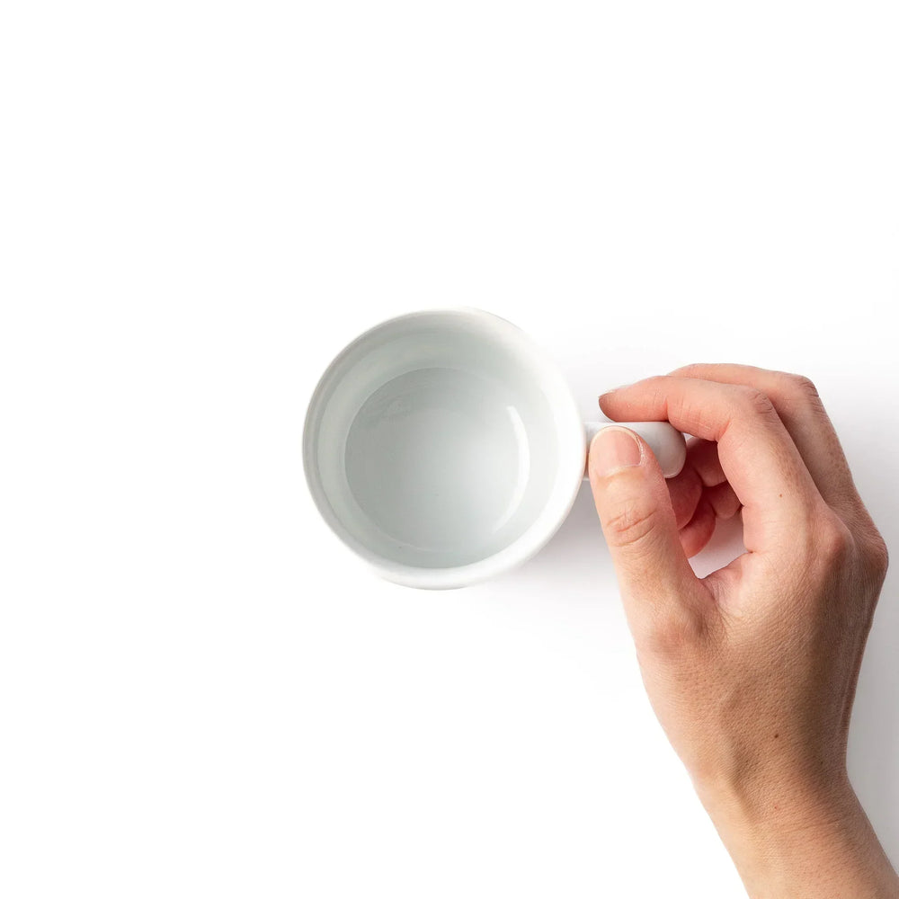 White ceramic kids mug with blue triceratops graphic, yellow horns and stripes, plus blue cloud accents, round handle.
