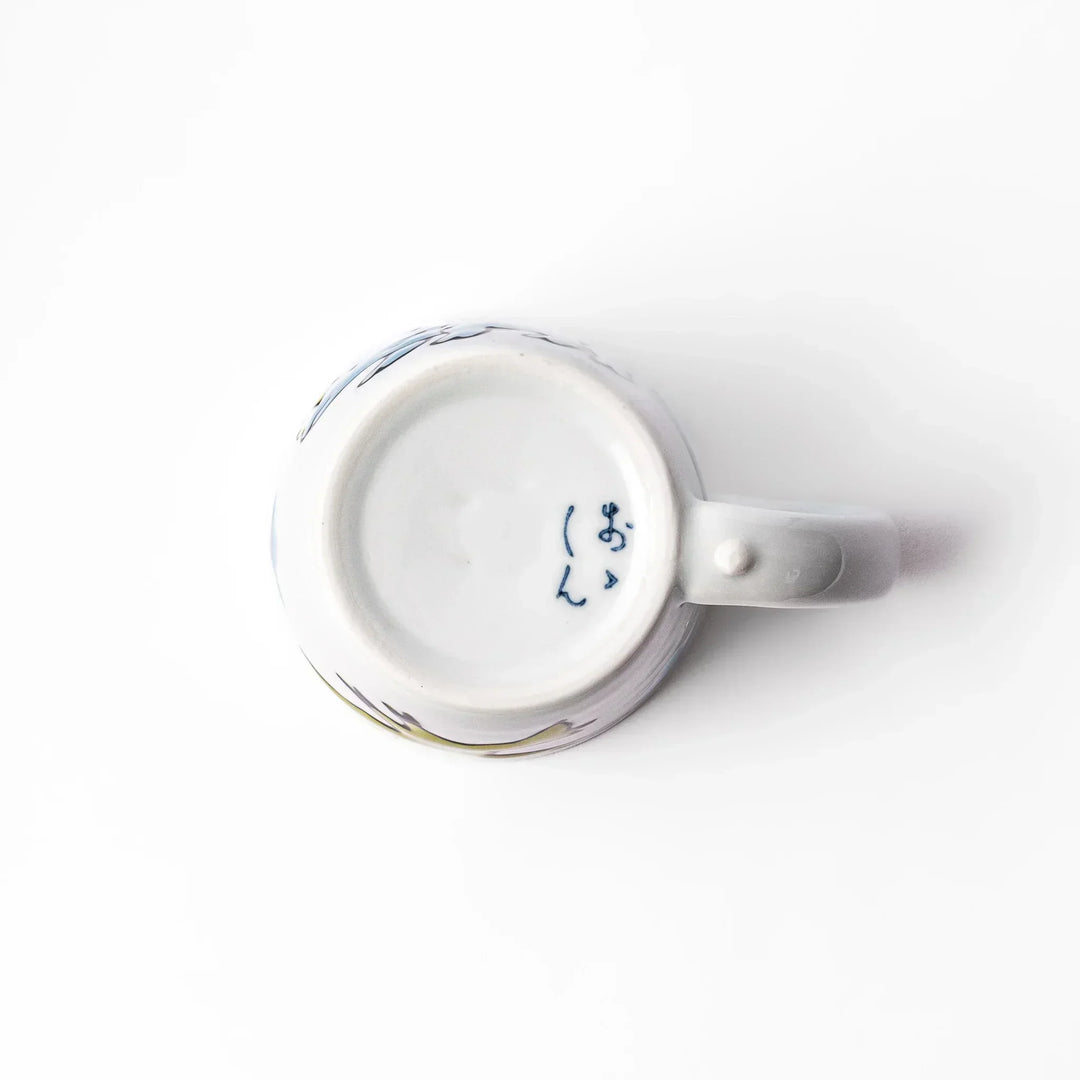 White ceramic kids mug with blue triceratops graphic, yellow horns and stripes, plus blue cloud accents, round handle.