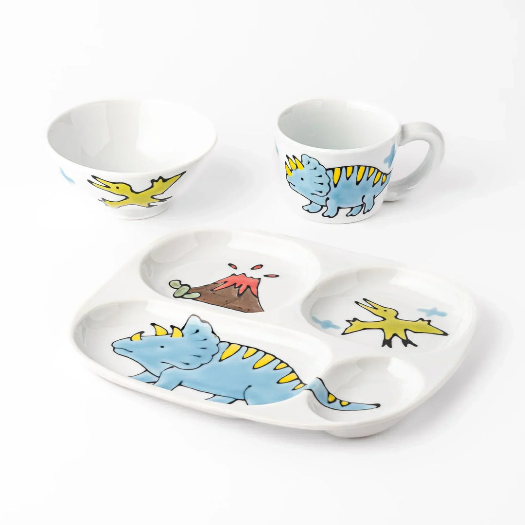 White ceramic kids mug, rice bowl and divided plate with blue triceratops, yellow pterodactyl, red volcano and blue clouds