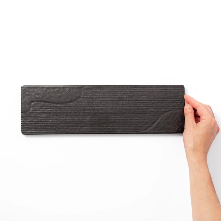 Rectangular black Japanese ceramic serving plate with subtle ridged woodgrain texture for modern dining.