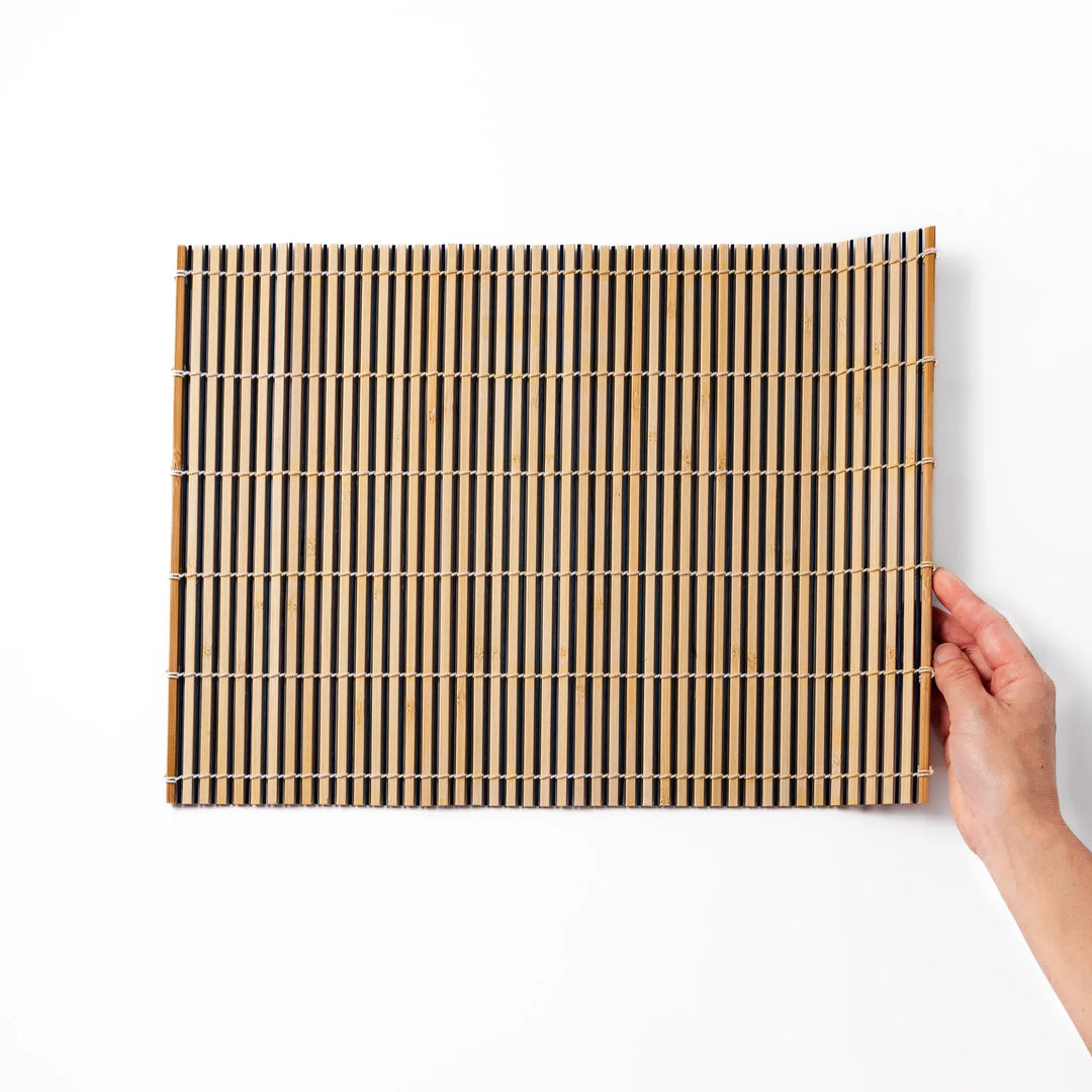 Two tone bamboo table mat with light and dark slats woven with white cord for textured Japanese dining.