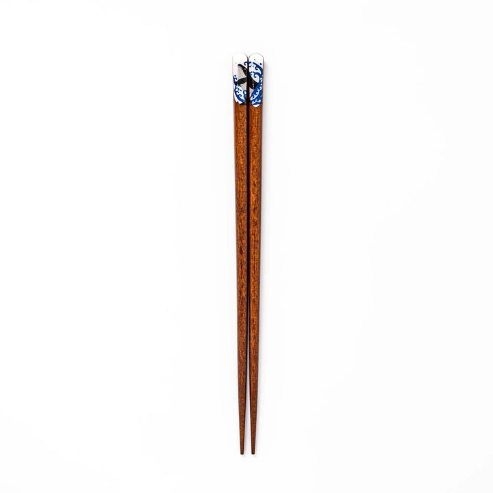 Pair of brown wooden chopsticks with white ceramic tips featuring a blue wave and whale design on a white background.