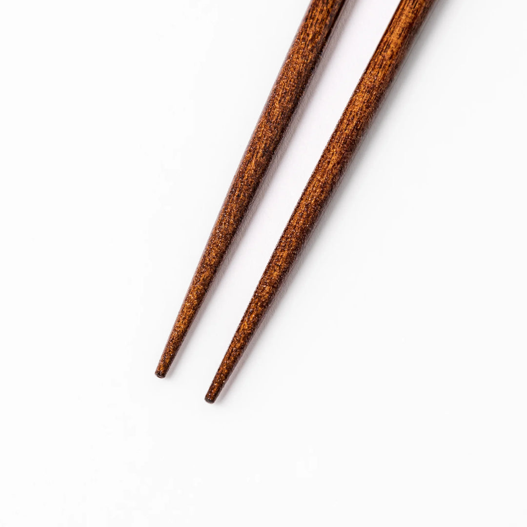 Pair of brown wooden chopsticks with white ceramic tips featuring a blue wave and whale design on a white background.