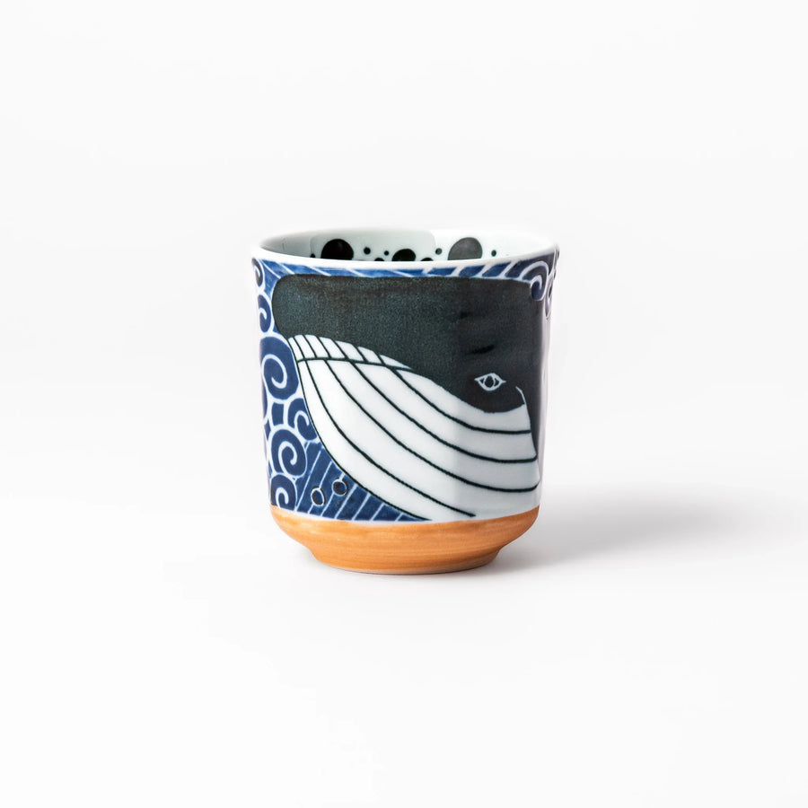 Porcelain tea cup featuring a bold black-and-white whale design surrounded by blue ocean waves with an unglazed brown base.