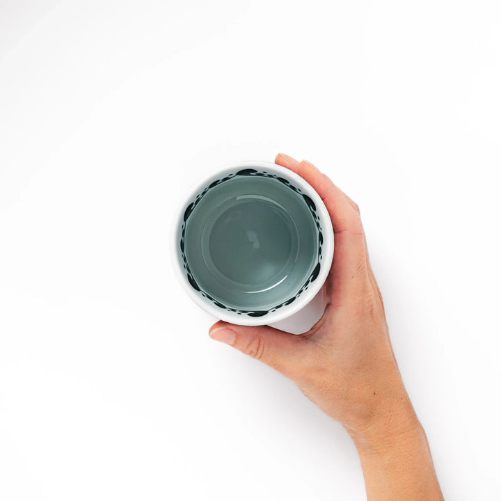 Porcelain tea cup featuring a bold black-and-white whale design surrounded by blue ocean waves with an unglazed brown base.