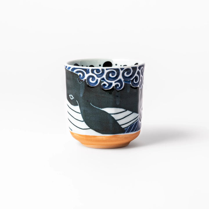 Porcelain tea cup featuring a bold black-and-white whale design surrounded by blue ocean waves with an unglazed brown base.