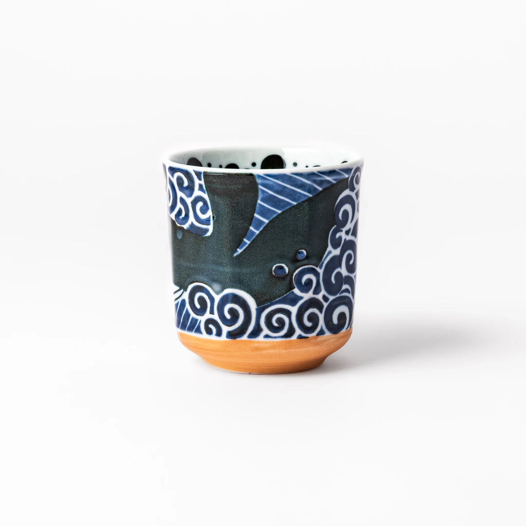 Porcelain tea cup featuring a bold black-and-white whale design surrounded by blue ocean waves with an unglazed brown base.
