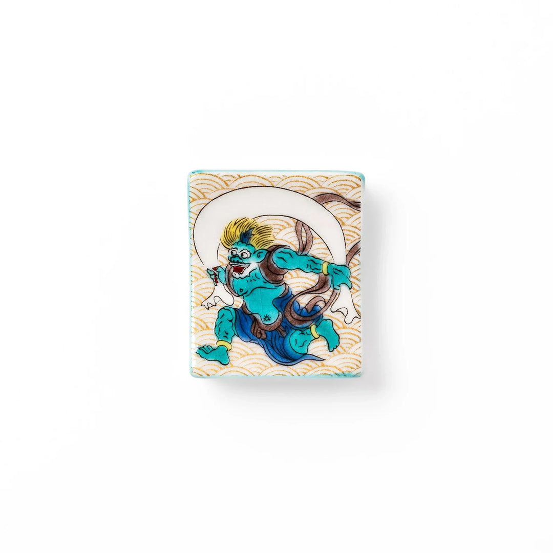 Japanese porcelain chopstick rest featuring the Wind God design with blue figure and gold wave pattern background.