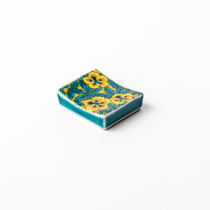 Rectangular Japanese ceramic chopstick rest with yellow floral design and teal leaves for elegant dining.