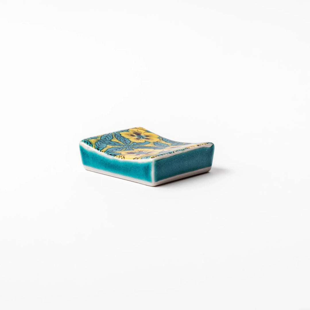 Rectangular Japanese ceramic chopstick rest with yellow floral design and teal leaves for elegant dining.