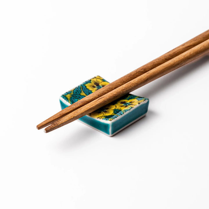 Rectangular Japanese ceramic chopstick rest with yellow floral design and teal leaves for elegant dining.