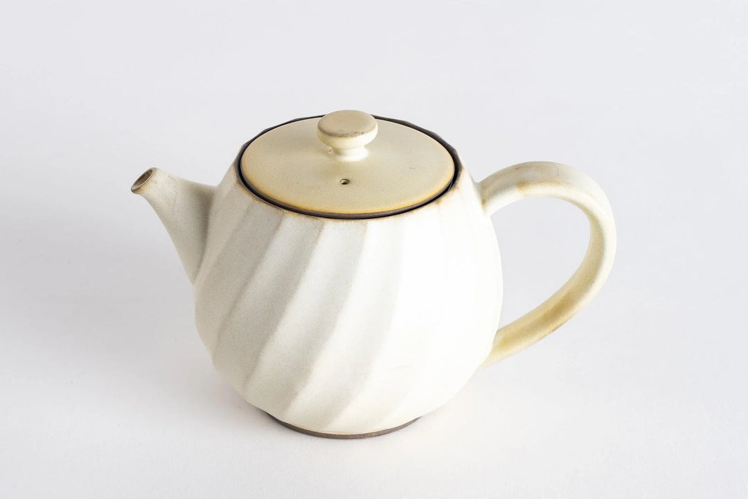 Elegant cream ceramic teapot with soft spiral design and rounded handle on a clean white background