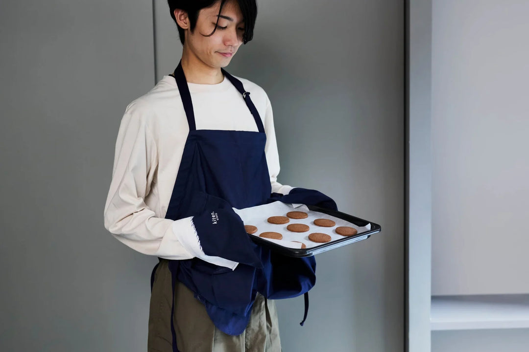 Man holding a tray of freshly baked cookies in a modern kitchen with plates and mugs set on the table
