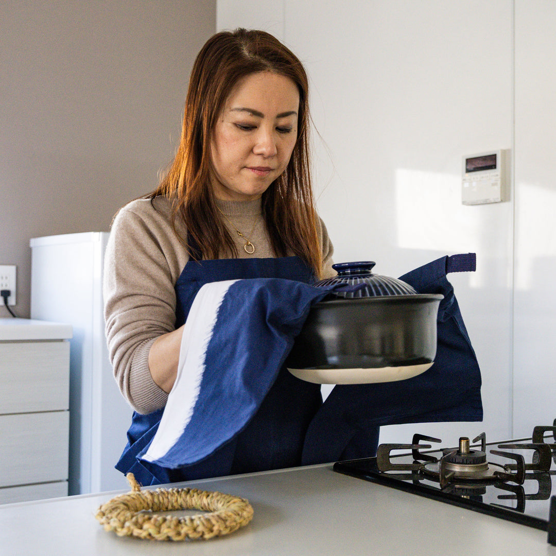 Nami from Just One Cookbook holding donabe pot with navy apron and built in mitten pocket