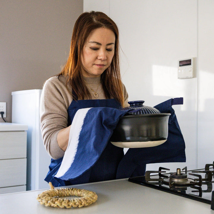 Nami from Just One Cookbook holding donabe pot with navy apron and built in mitten pocket