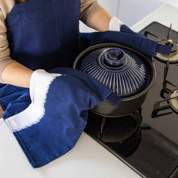 Nami from Just One Cookbook lifting donabe from stovetop using apron hem pocket as mitten